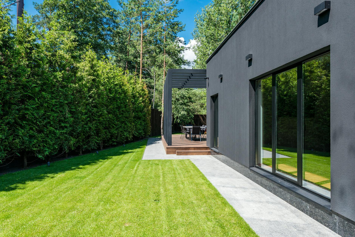 Stylish modern house exterior with a lush green yard and outdoor seating area.
