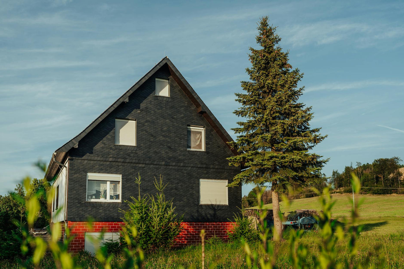Charming rural home with brick base and a tall pine tree under a clear summer sky.