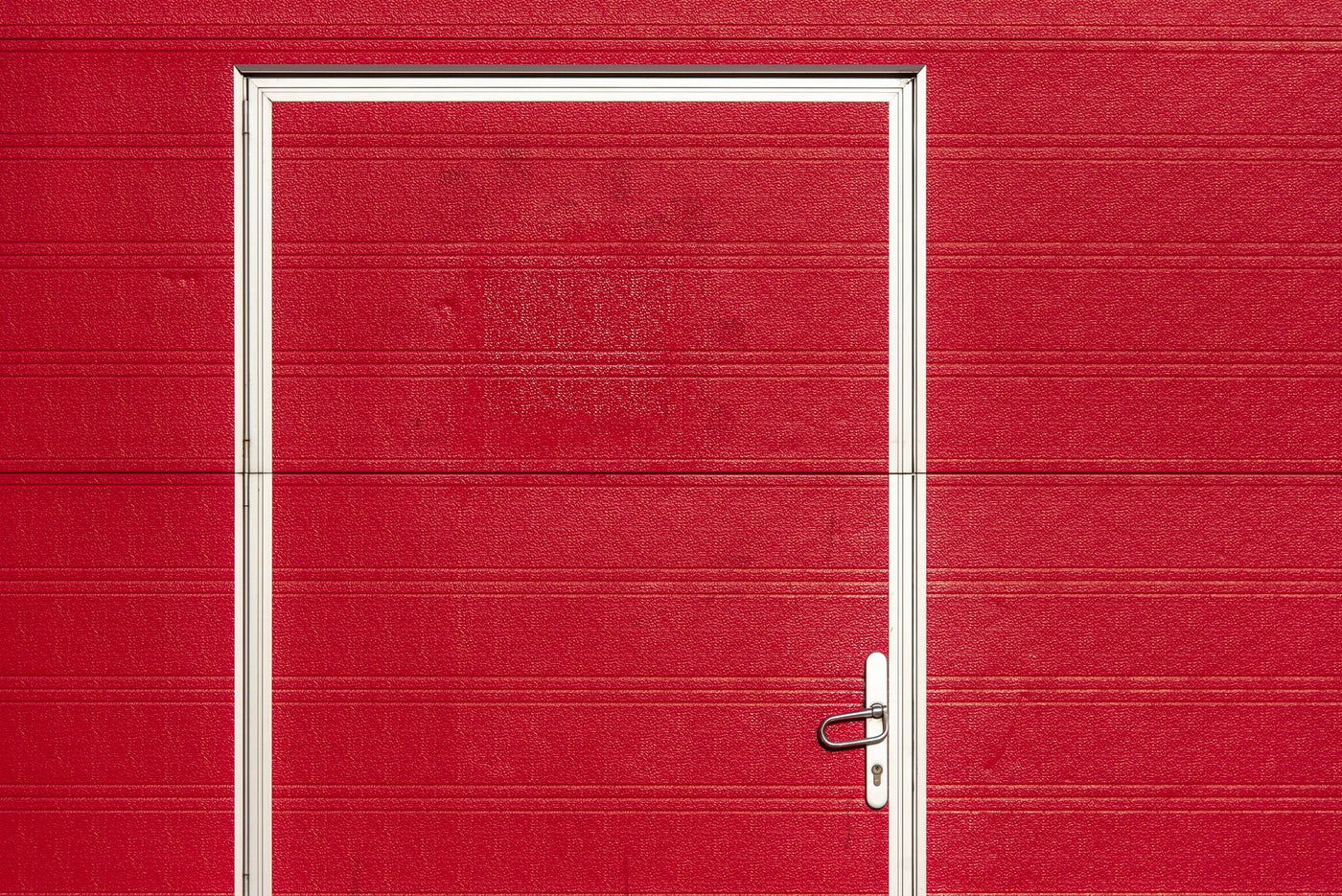 Minimalist image of a bold red garage door with a white frame and textured surface.