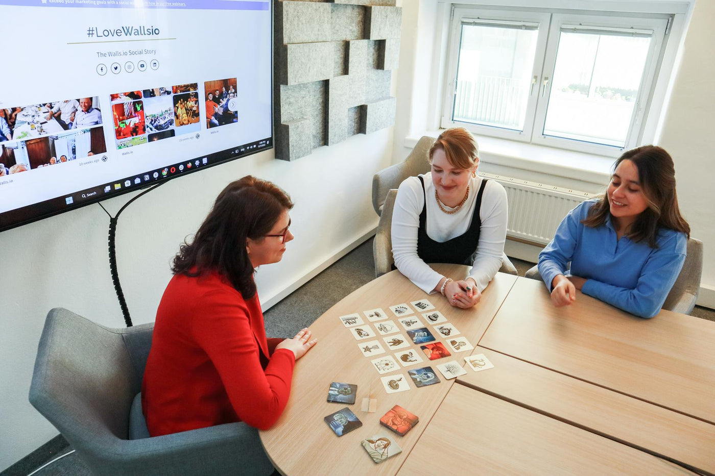 Three women playing a card game in a modern office setting, enjoying team building time.